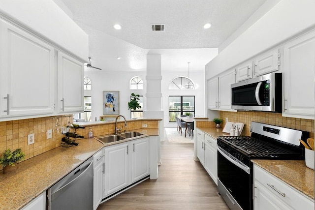 7419 Dallas Dr, Austin, TX 78729 - kitchen with appliances with stainless steel finishes, a sink, a peninsula, white cabinets, and light wood finished floors