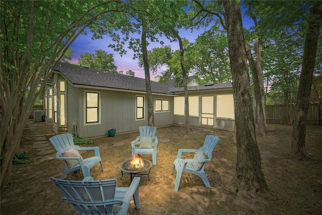 back of property at dusk featuring fence private yard, a shingled roof, an outdoor fire pit, and central AC