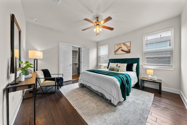 bedroom featuring ceiling fan, a walk in closet, baseboards, wood finished floors, and a closet