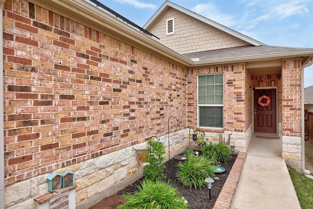 entrance to property with brick siding and a shingled roof