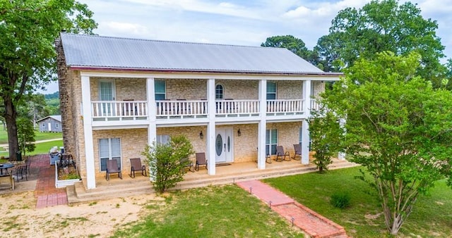 rear view of house with a balcony, stone siding, a patio, metal roof, and a lawn