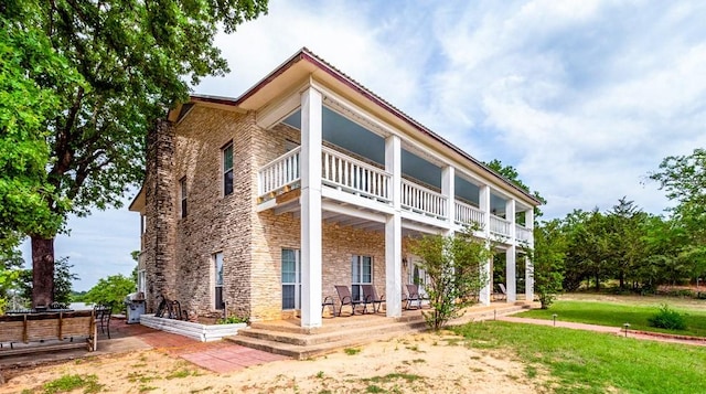 back of property with a yard, a balcony, and stone siding