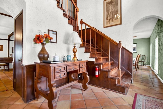 staircase featuring arched walkways, a textured wall, and tile patterned floors
