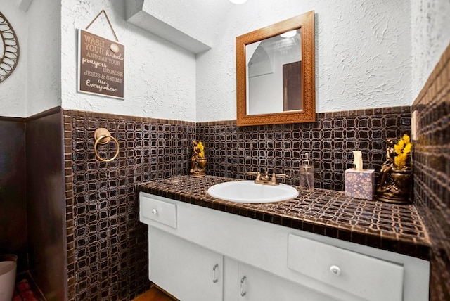 bathroom with vanity, a textured wall, wainscoting, and tile walls