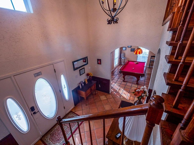 tiled foyer with a textured wall, a high ceiling, arched walkways, stairs, and pool table