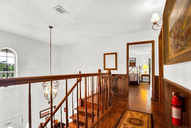 corridor featuring wood-type flooring, visible vents, wainscoting, a textured ceiling, and a notable chandelier