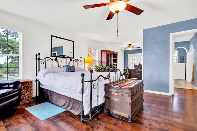 bedroom featuring baseboards, a textured wall, arched walkways, and wood finished floors