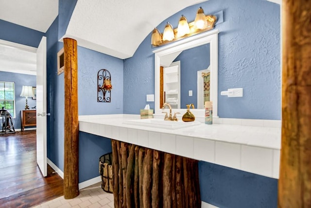 bathroom with vanity, a textured wall, vaulted ceiling, and wood finished floors
