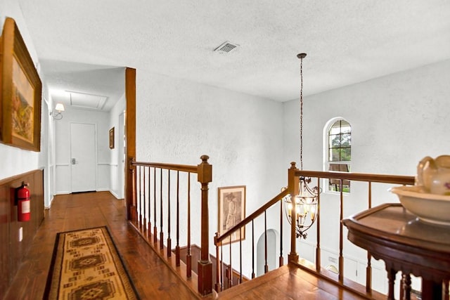hallway with a textured ceiling, a textured wall, hardwood / wood-style floors, and an upstairs landing