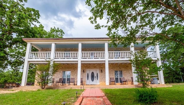 rear view of property featuring a yard, a balcony, stone siding, and covered porch