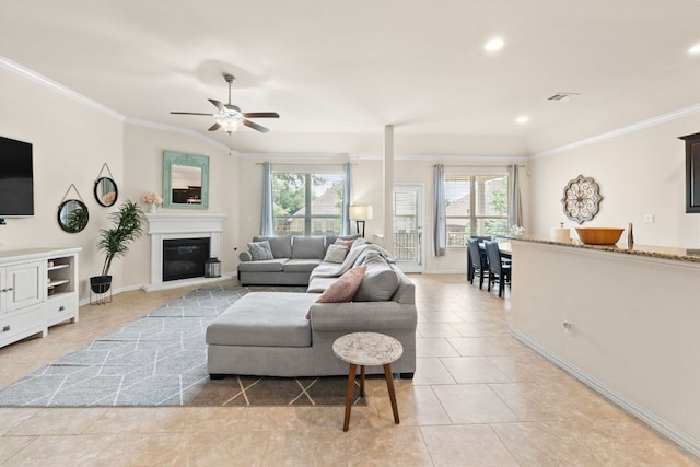 living room with a glass covered fireplace, ornamental molding, ceiling fan, and a wealth of natural light