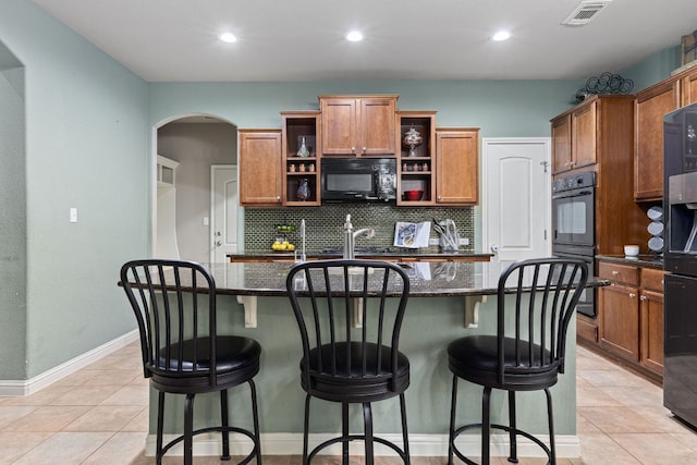 kitchen with decorative backsplash, arched walkways, open shelves, black appliances, and an island with sink