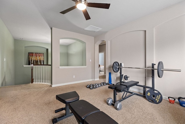 exercise area featuring carpet floors, visible vents, baseboards, ceiling fan, and arched walkways
