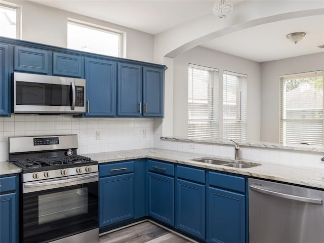 kitchen with a sink, appliances with stainless steel finishes, blue cabinets, and arched walkways
