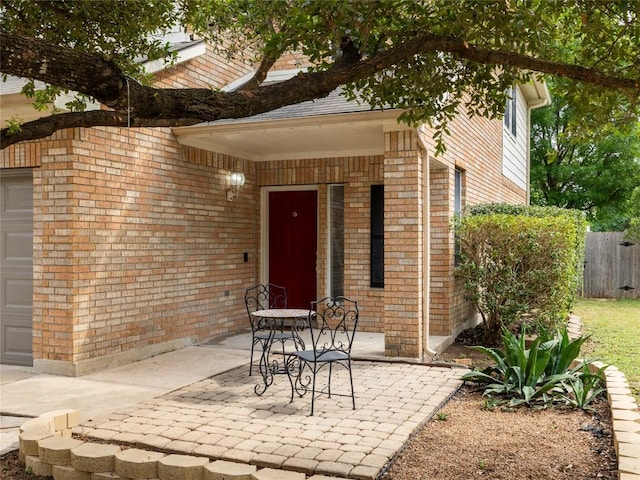 entrance to property featuring brick siding, fence, and a patio