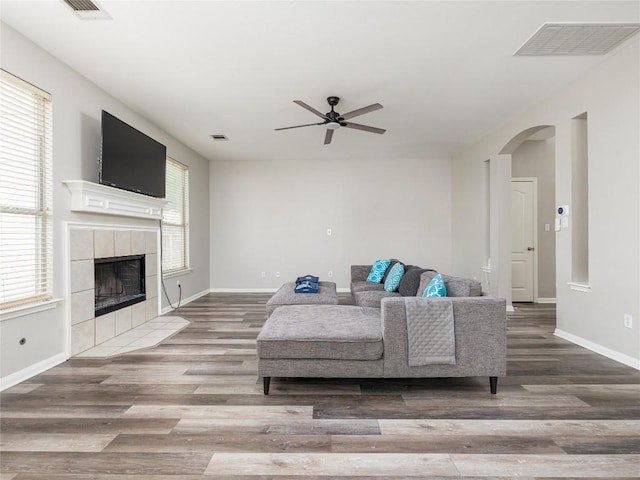 living room featuring a tiled fireplace, a ceiling fan, wood finished floors, and visible vents