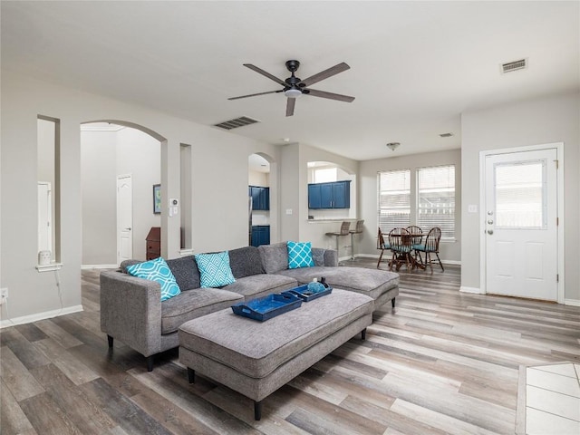 living room featuring visible vents, arched walkways, light wood-style floors, and ceiling fan