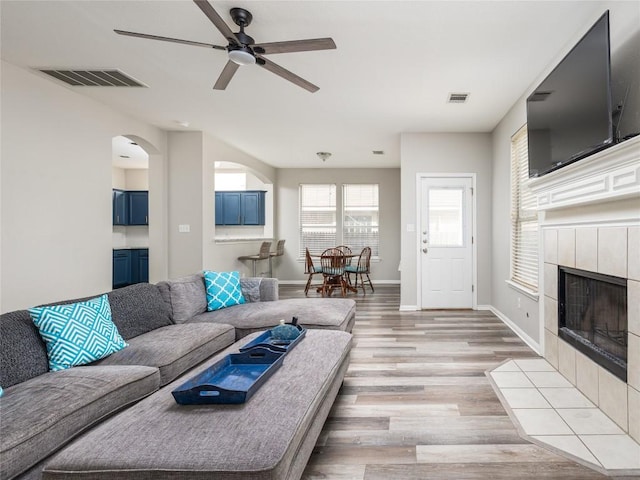 living room with visible vents, a ceiling fan, light wood-style floors, and a fireplace