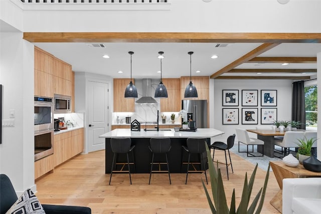 kitchen featuring wall chimney range hood, appliances with stainless steel finishes, modern cabinets, and a kitchen breakfast bar