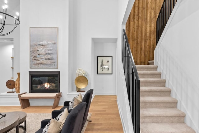 stairs featuring wood finished floors, a glass covered fireplace, a high ceiling, and a chandelier
