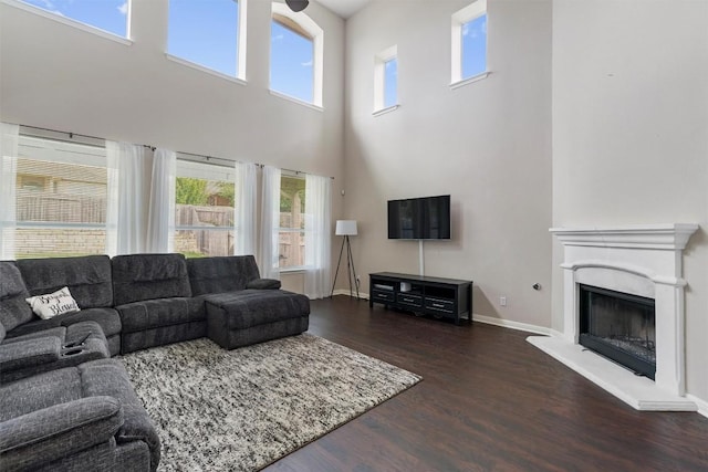 living room with wood finished floors, a high ceiling, baseboards, and a fireplace with raised hearth