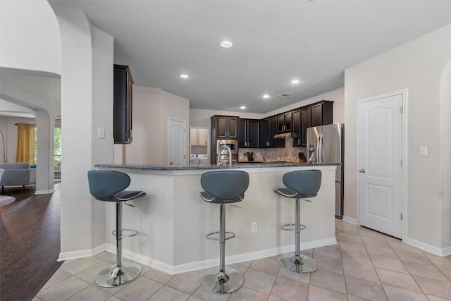 kitchen with stainless steel refrigerator with ice dispenser, arched walkways, a kitchen breakfast bar, light tile patterned flooring, and recessed lighting