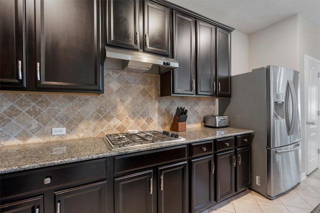 kitchen with under cabinet range hood, appliances with stainless steel finishes, light stone countertops, and light tile patterned floors