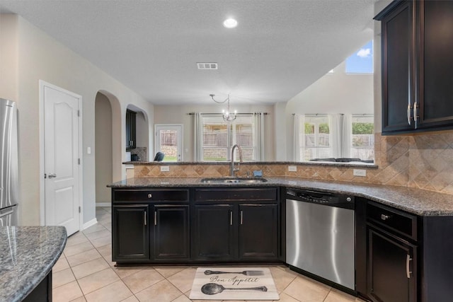 kitchen with appliances with stainless steel finishes, a sink, decorative backsplash, and dark stone counters