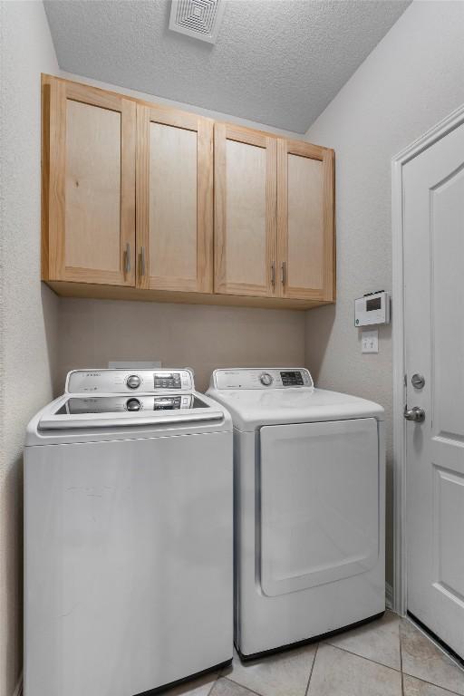 washroom with cabinet space, washer and clothes dryer, a textured ceiling, and light tile patterned floors