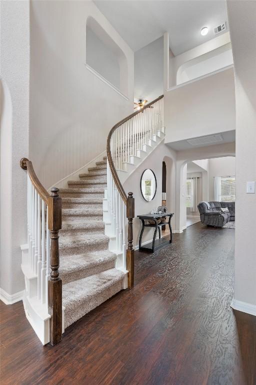 stairway featuring wood finished floors, arched walkways, baseboards, and a high ceiling