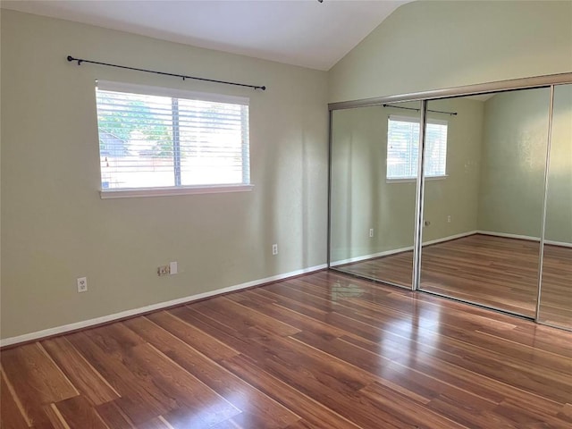 unfurnished bedroom featuring multiple windows, wood finished floors, lofted ceiling, and a closet