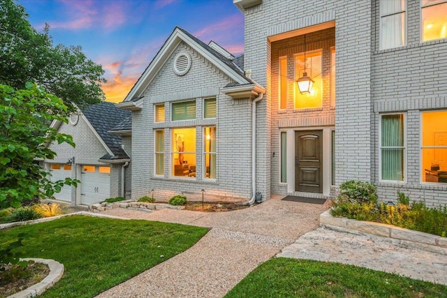 exterior entry at dusk featuring a yard and brick siding
