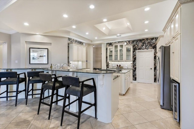 kitchen with a raised ceiling, beverage cooler, freestanding refrigerator, a peninsula, and a kitchen bar
