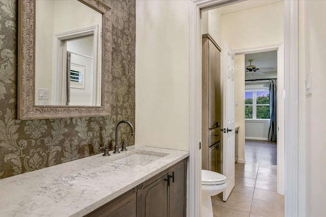 bathroom with vanity, toilet, tile patterned floors, baseboards, and wallpapered walls
