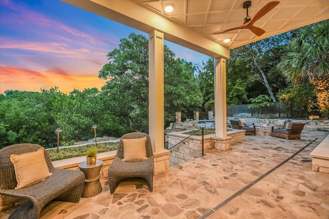 patio terrace at dusk featuring fence, a ceiling fan, and a fire pit