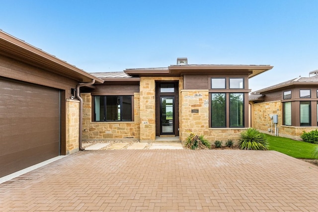 2317 Kahala Sunset Dr, Spicewood, TX 78669 - view of exterior entry featuring a standing seam roof, metal roof, decorative driveway, an attached garage, and stone siding