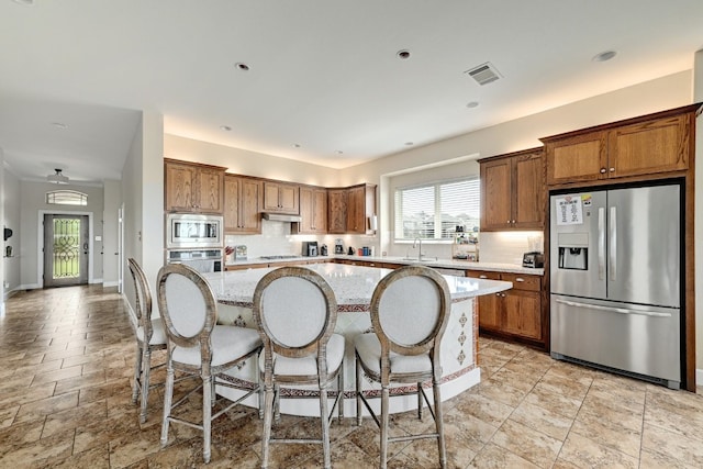 kitchen with a sink, brown cabinetry, a center island, stainless steel appliances, and under cabinet range hood