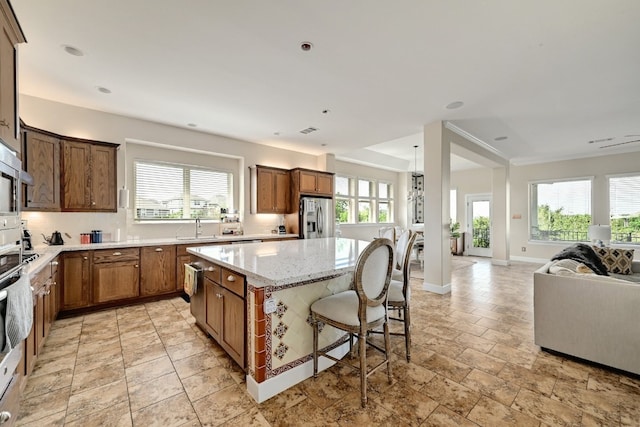 kitchen featuring a kitchen island, light stone countertops, open floor plan, stainless steel fridge with ice dispenser, and a sink
