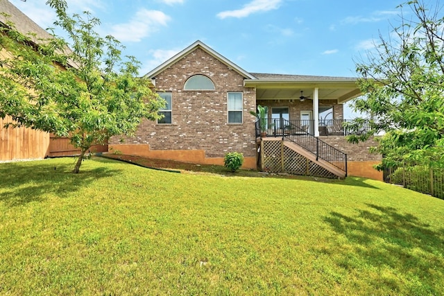 back of house with a lawn, a ceiling fan, stairs, and brick siding