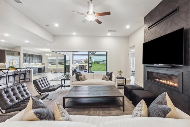living area with visible vents, ceiling fan, wood finished floors, and a large fireplace