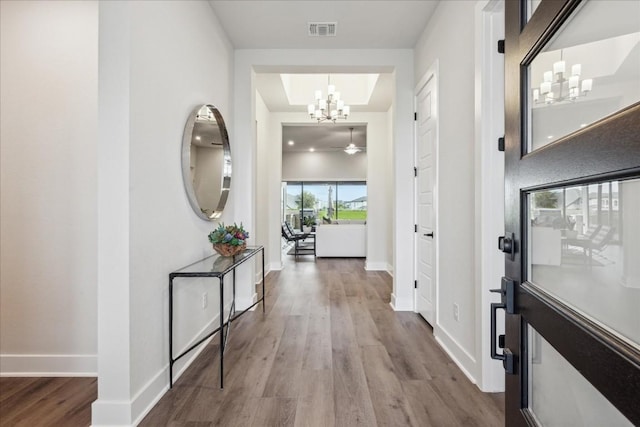hall with baseboards, a notable chandelier, wood finished floors, and visible vents