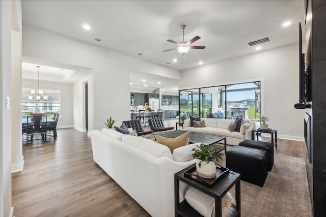 living area featuring a healthy amount of sunlight, ceiling fan with notable chandelier, wood finished floors, and visible vents
