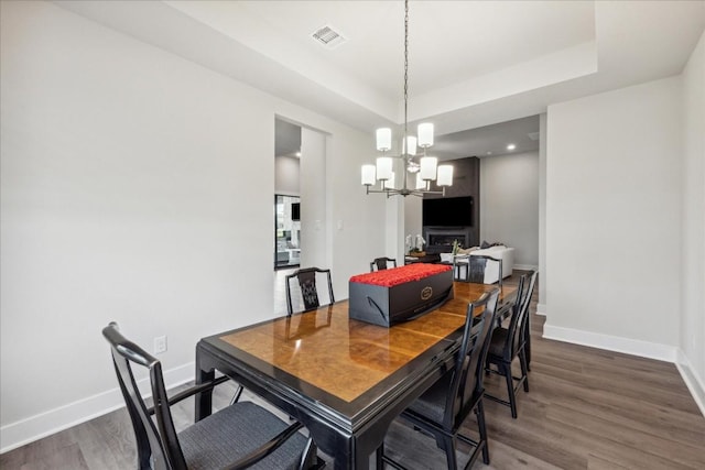dining space featuring an inviting chandelier, visible vents, baseboards, dark wood-style floors, and a tray ceiling
