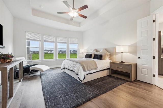 bedroom featuring a ceiling fan, a raised ceiling, and wood finished floors