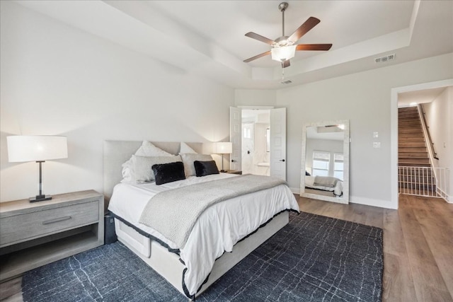 bedroom featuring visible vents, wood finished floors, baseboards, a raised ceiling, and a ceiling fan