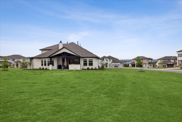 exterior space featuring stone siding, a chimney, a shingled roof, a lawn, and a residential view