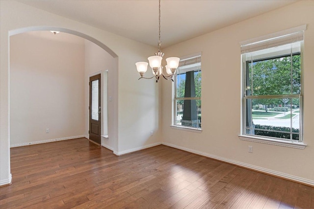 spare room with arched walkways, wood finished floors, and a wealth of natural light