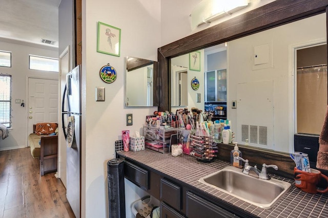 kitchen featuring a sink, light wood-style floors, tile counters, freestanding refrigerator, and visible vents