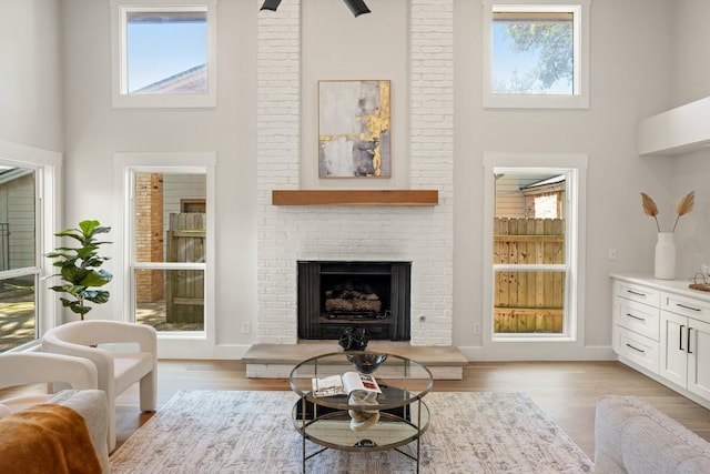 living area with a fireplace, light wood finished floors, and a towering ceiling
