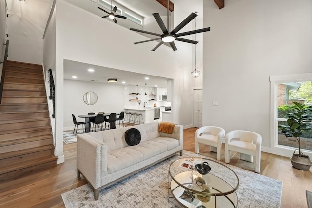 living room with ceiling fan, light wood-style floors, stairs, baseboards, and a towering ceiling